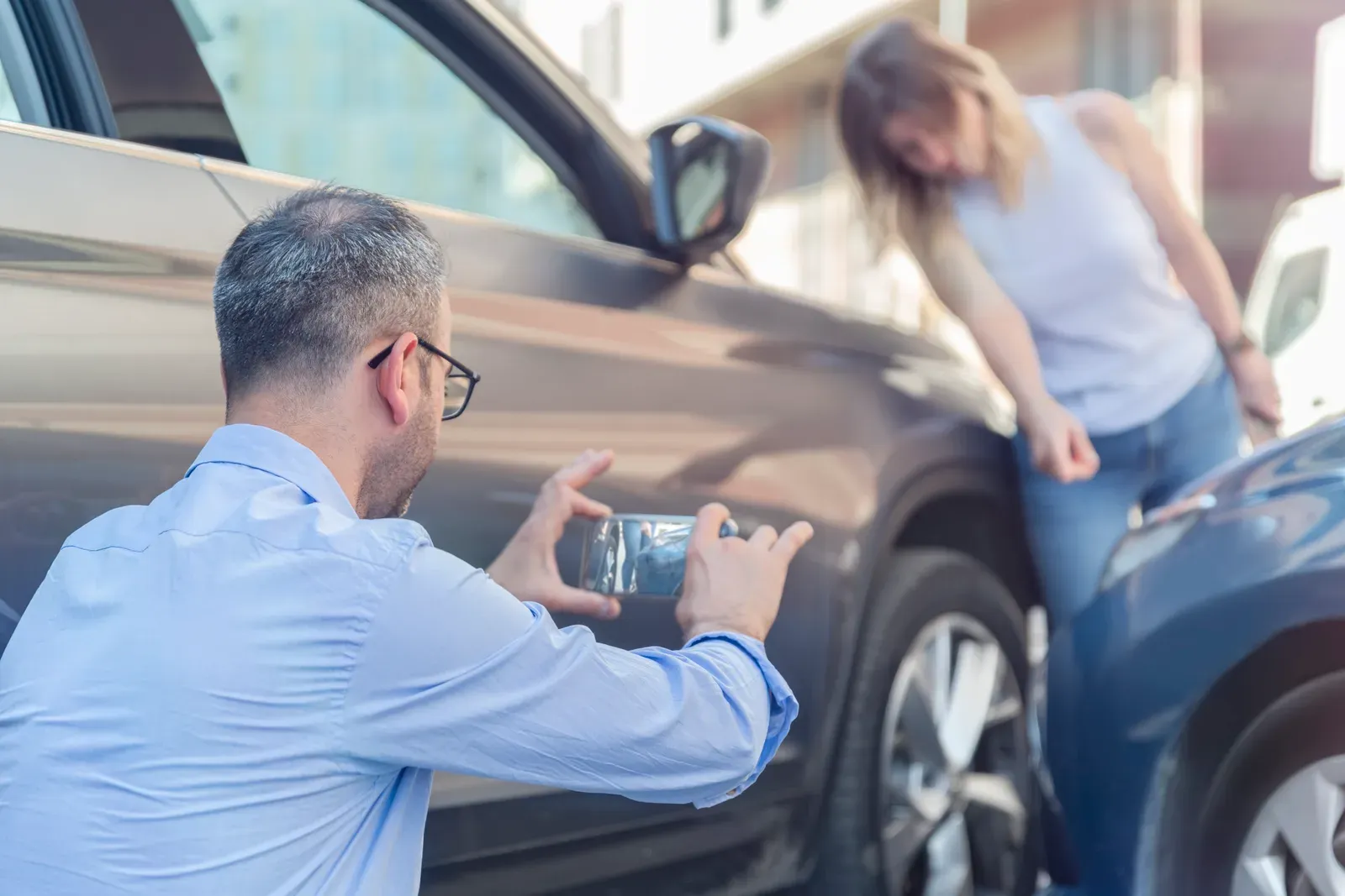 A man photographing door damage with his phone while a woman inspects the car