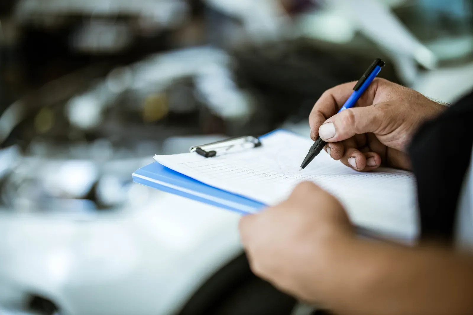 A hand filling out a repair checklist on a clipboard beside a car