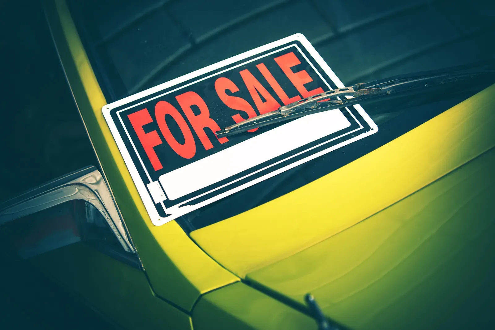 A red and white for-sale sign tucked under the wiper of a yellow classic car