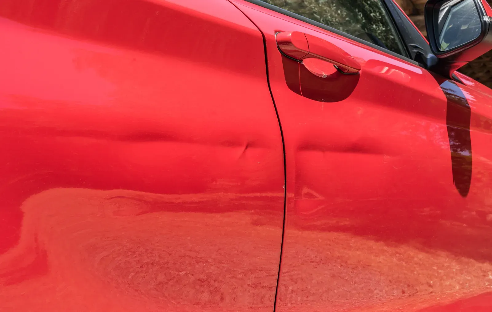 Shallow dents creasing a red front door and fender below the handle line