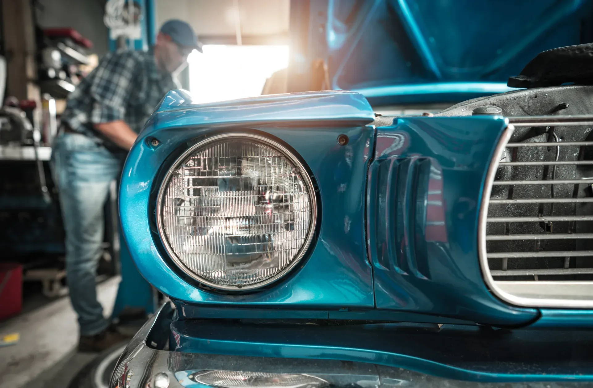 Close-up of a teal classic car's round headlight and grille inside a workshop