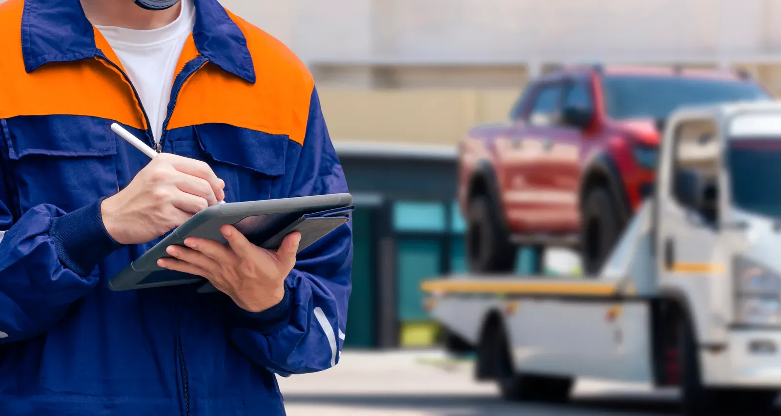 An insurance adjuster in uniform noting details on a tablet near a towed pickup
