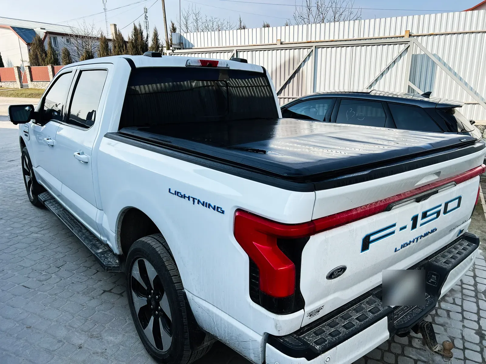 A white electric pickup truck with a black bed cover parked by a metal fence