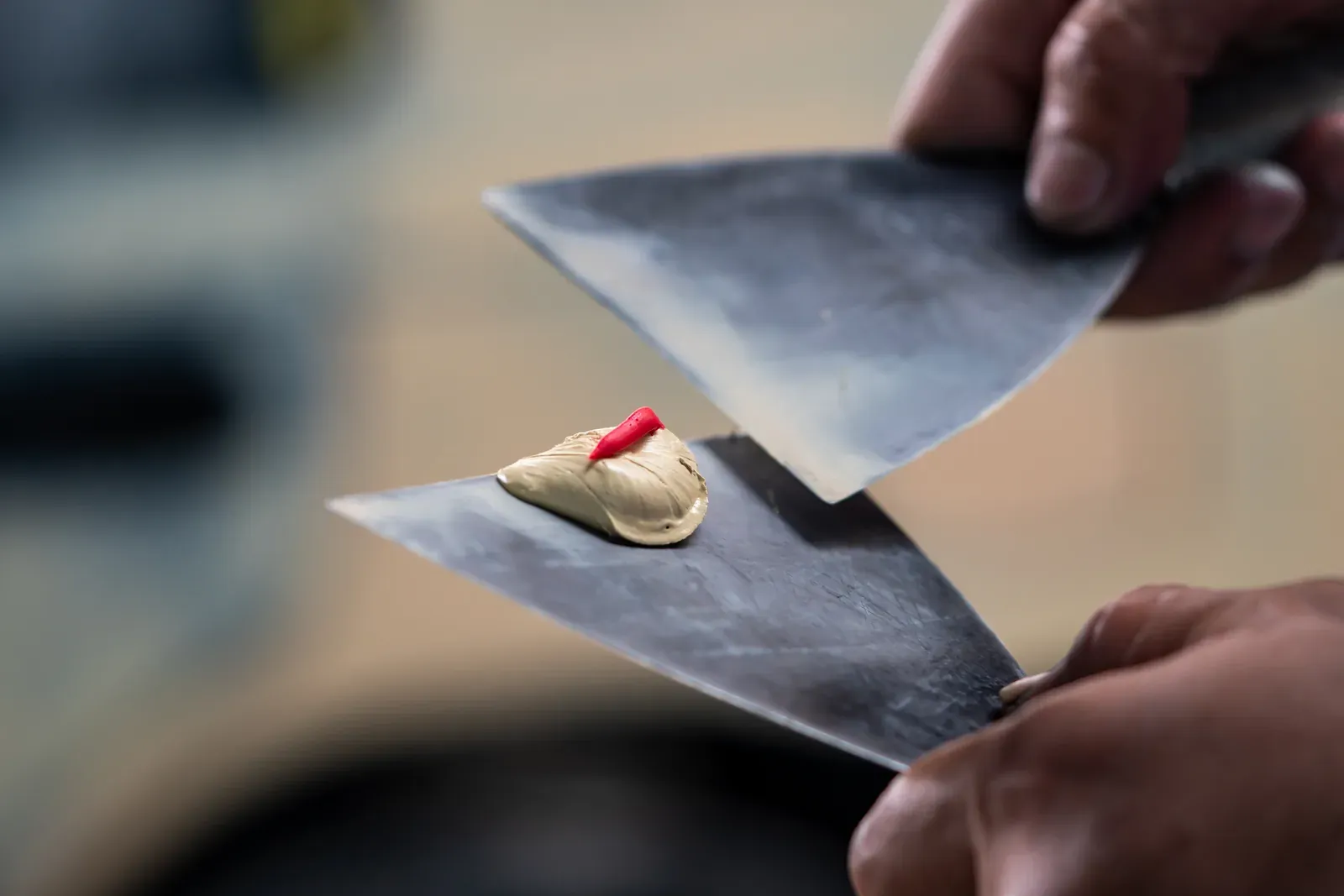 Two putty knives mixing beige body filler with a stripe of red hardener