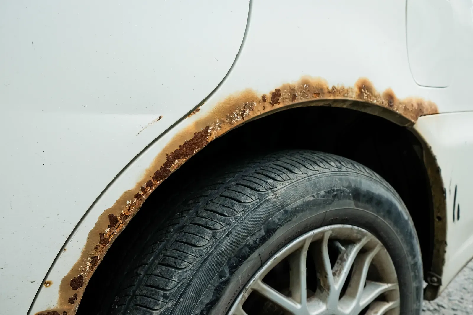 Heavy rust eating along the rear wheel arch of a white car