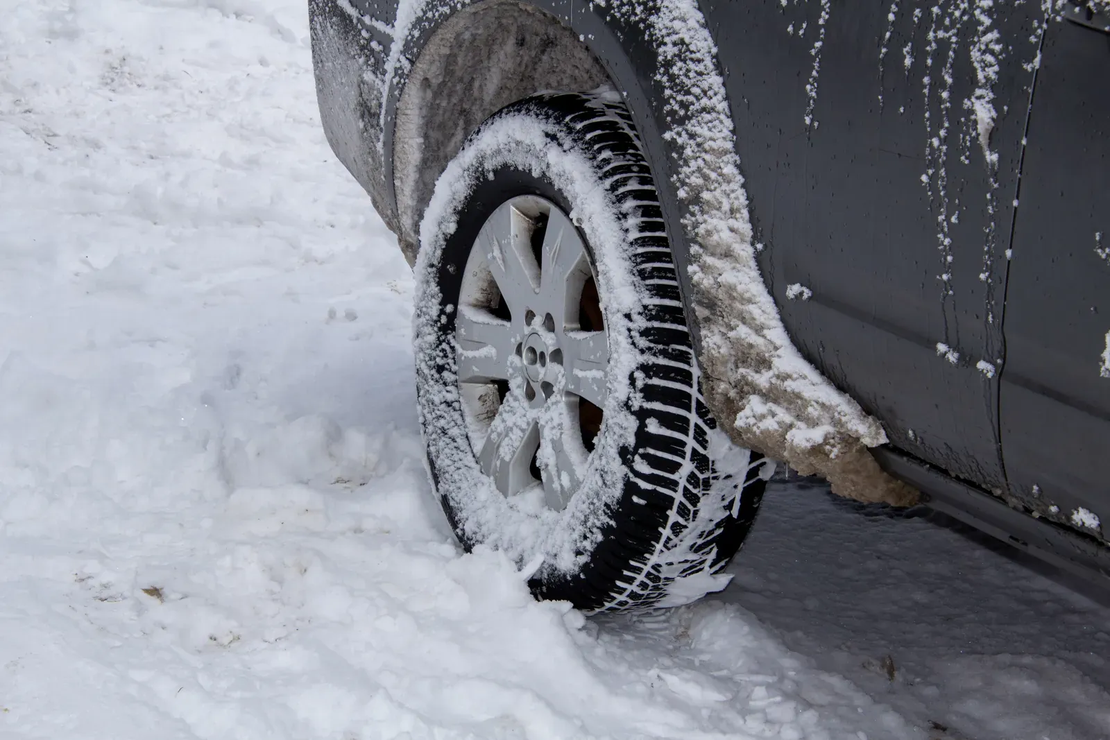 A snow-caked wheel and arch on a dark vehicle after winter driving