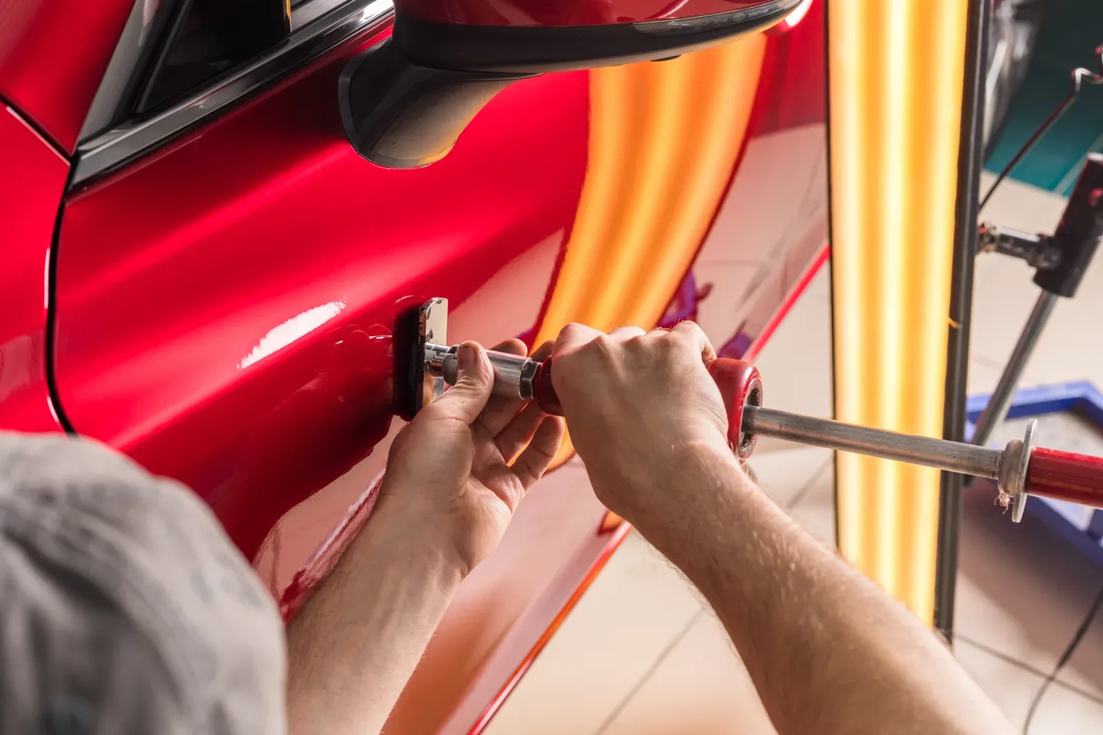 Hands using a slide hammer to pull a dent from a red door
