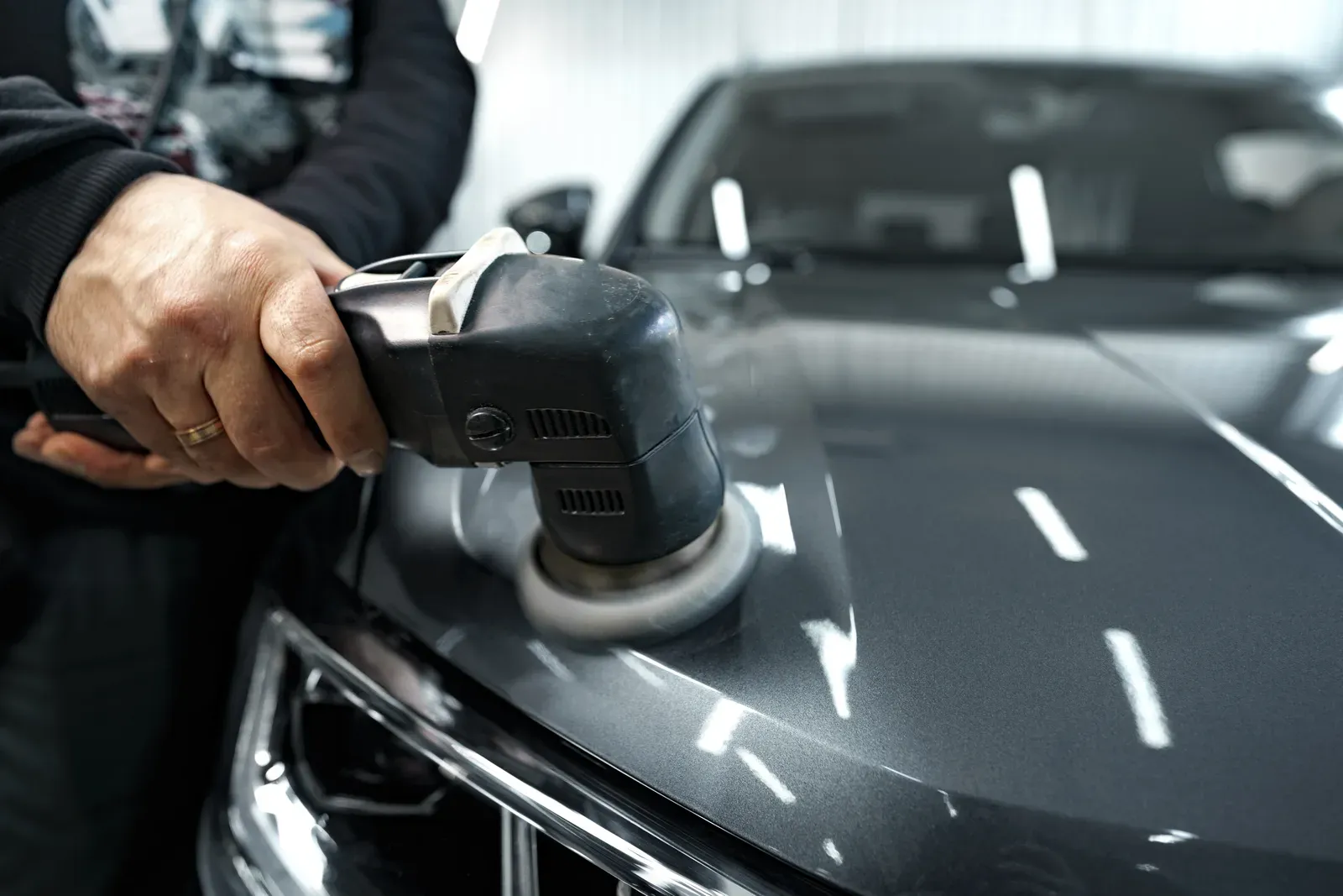 A polisher buffing the hood of a dark grey car to a mirror shine