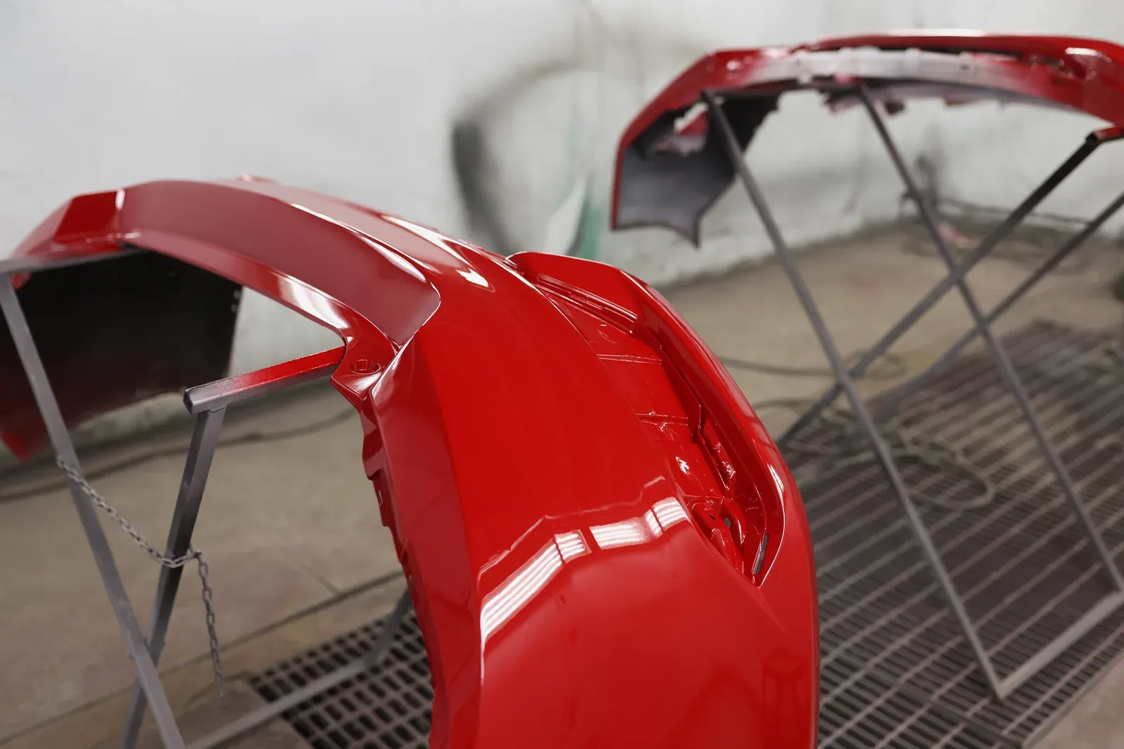 Two freshly painted glossy red bumpers drying on metal stands in a booth