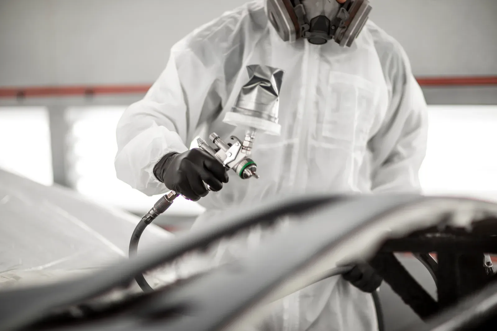 A painter holding a spray gun with a foil-wrapped cup beside a dark panel