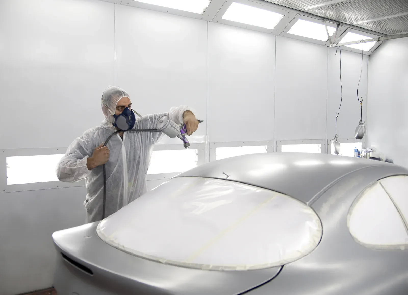 A hooded painter spraying a silver coupe with its windows masked white