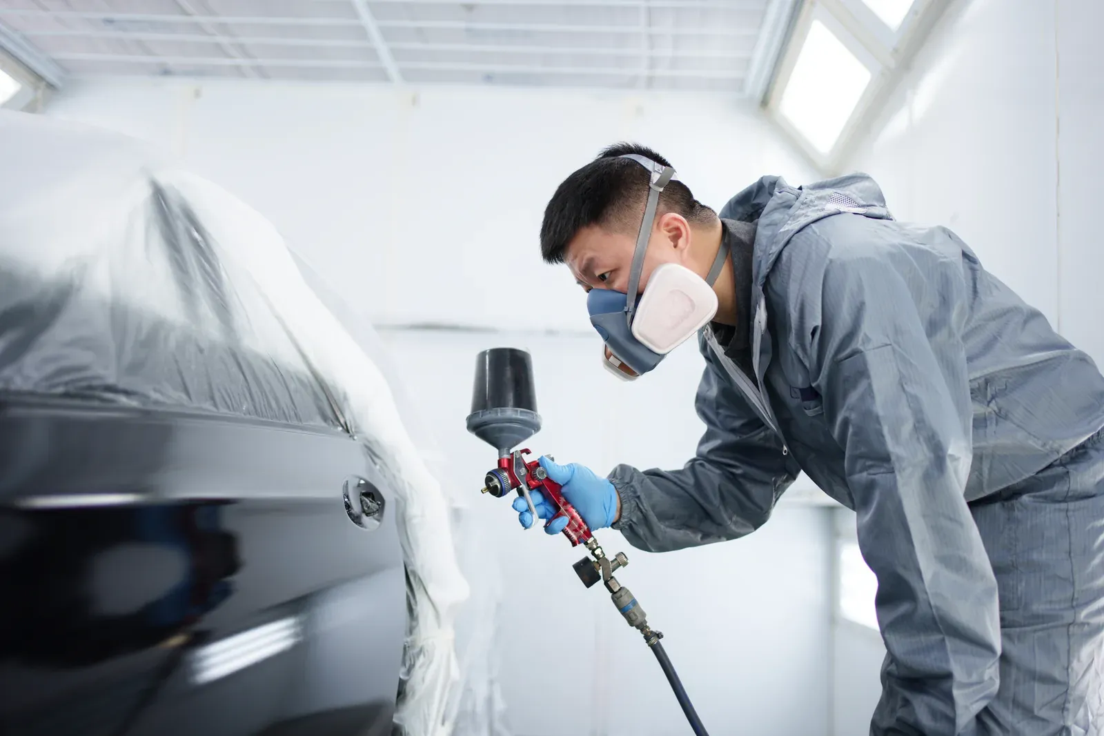 A painter leaning in to spray a glossy dark sedan with masked windows