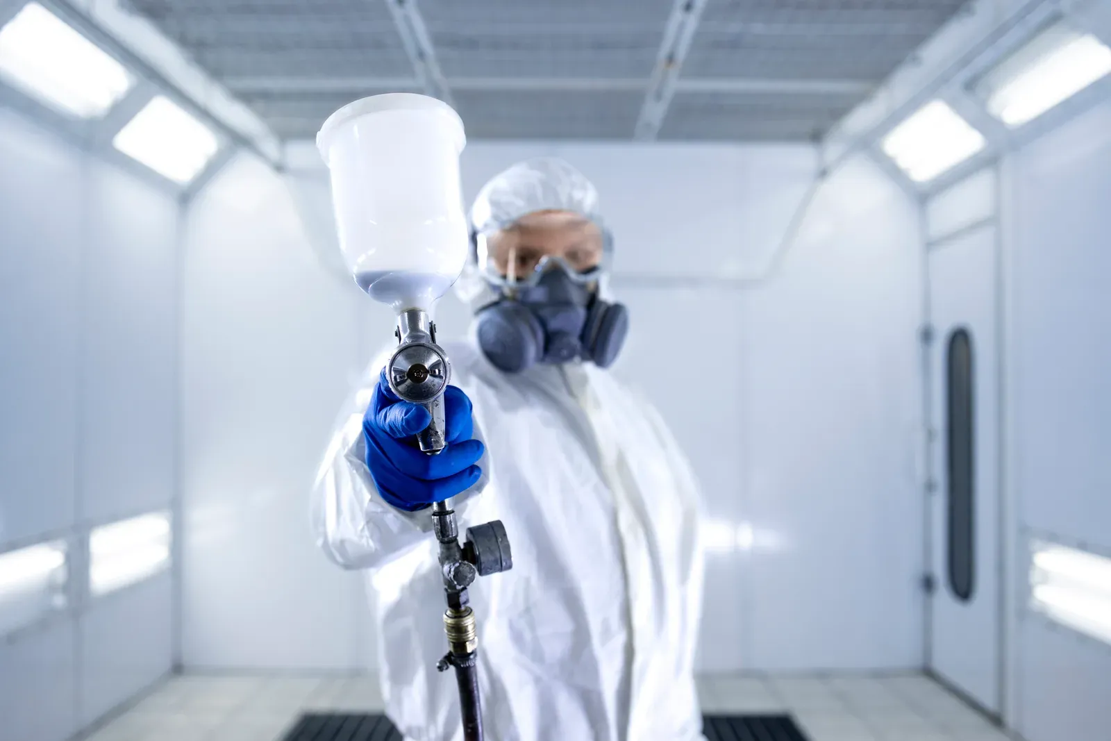 A painter in full protective gear pointing a spray gun toward the camera