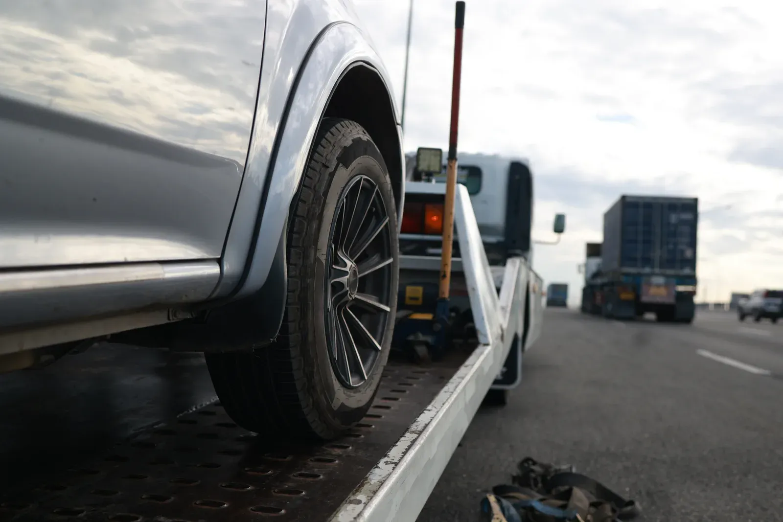 A silver SUV strapped on a flatbed tow truck deck along a highway